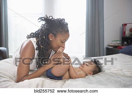 Mother kissing feet of baby daughter laying on bed View Large Photo Image Stock Image - Mother kissing feet of baby daughter laying on bed. Fotosearch