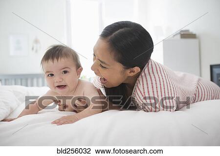 Stock Image - Mother playing on bed with baby son. Fotosearch