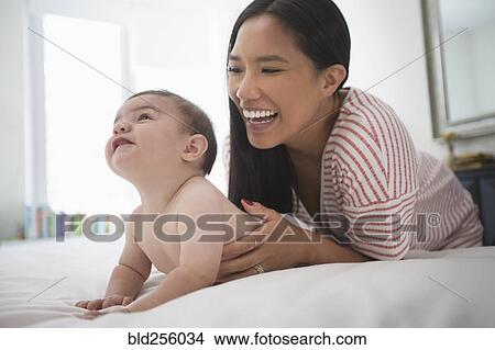 Picture - Mother playing with baby son laying on bed. Fotosearch