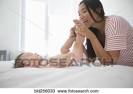 Mother playing with feet of baby son laying on bed View Large Photo Image Stock Image - Mother playing with feet of baby son laying on bed. Fotosearch