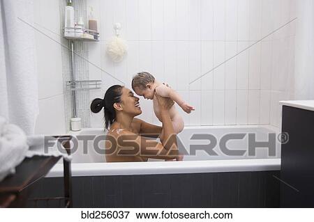 Stock Photo - Mother sitting in bathtub holding baby son. Fotosearch