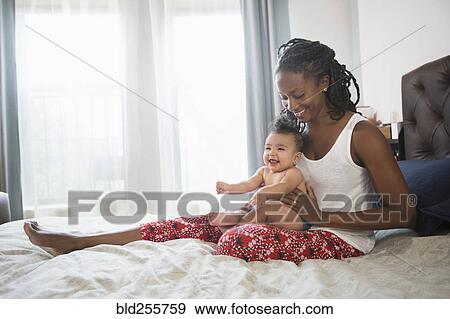 Stock Photo - Mother sitting on bed holding baby daughter on lap. Fotosearch