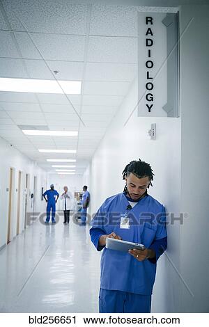 Stock Image - Nurse leaning on wall in hospital using digital tablet. Fotosearch