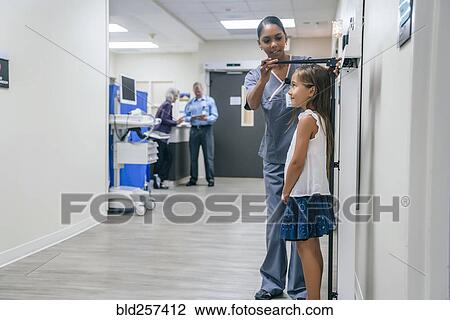 Stock Image - Nurse measuring height of girl in hospital. Fotosearch