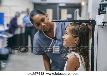 Stock Image - Nurse measuring height of girl in hospital. Fotosearch