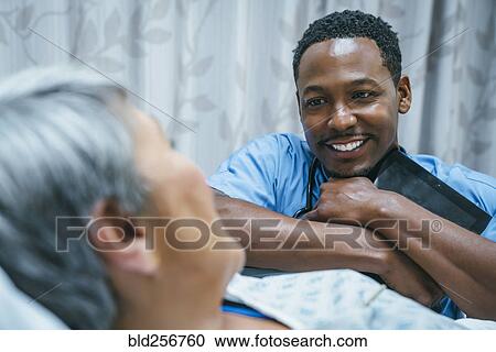 Stock Image - Nurse talking to patient in hospital bed. Fotosearch