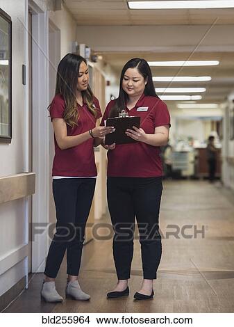 Picture - Nurses reading clipboard in hospital corridor. Fotosearch
