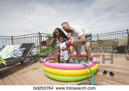 Picture - Parents posing for selfie with children in inflatable swimming pool. Fotosearch