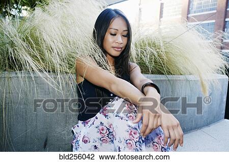 Pensive Asian woman sitting near foliage View Large Photo Image Stock Image - Pensive Asian woman sitting near foliage. Fotosearch