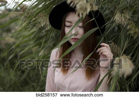 Stock Photo - Pensive Asian woman standing in field of tall grass. Fotosearch