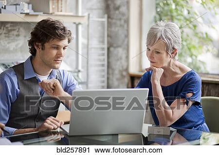 Stock Image - Pensive businesspeople using laptop in office. Fotosearch