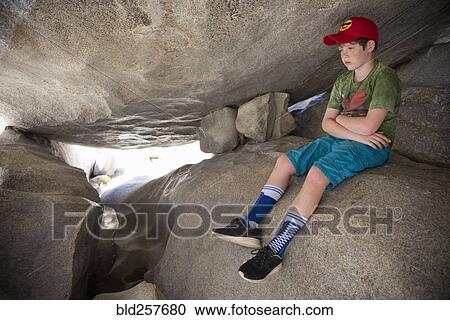 Stock Image - Pensive Caucasian boy sitting on rocks. Fotosearch