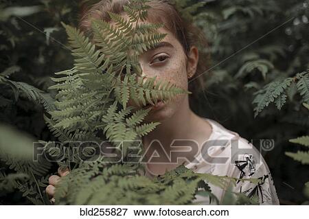 Stock Photo - Pensive Caucasian girl behind green leaves. Fotosearch