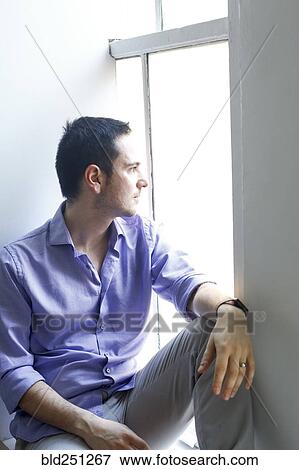 Stock Photo - Pensive Caucasian man sitting on windowsill. Fotosearch