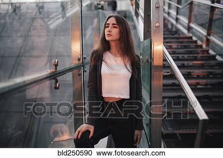 Stock Image - Pensive Caucasian woman at window near staircase. Fotosearch