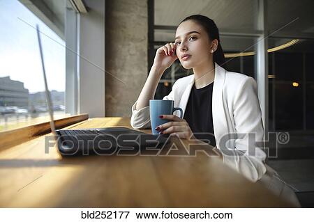 Pensive Caucasian woman drinking coffee near laptop View Large Photo Image Stock Photo - Pensive Caucasian woman drinking coffee near laptop. Fotosearch