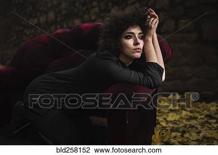Stock Image - Pensive Caucasian woman laying on sofa outdoors. Fotosearch