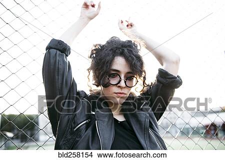 Picture - Pensive Caucasian woman leaning on chain-link fence. Fotosearch