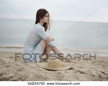 Stock Image - Pensive Caucasian woman sitting on beach. Fotosearch