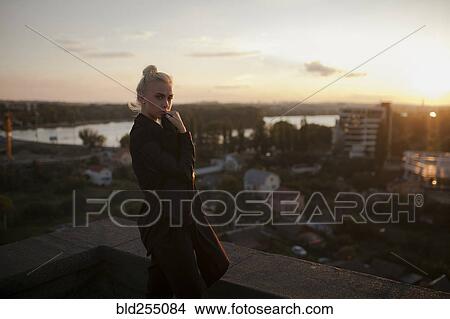 Picture - Pensive Caucasian woman standing on roof at sunset. Fotosearch