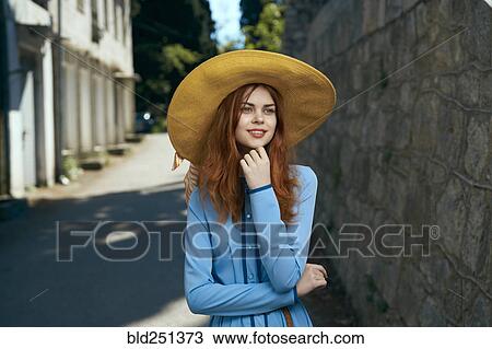 Stock Image - Pensive Caucasian woman wearing hat near stone wall. Fotosearch
