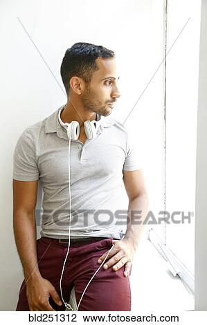 Stock Image - Pensive mixed race man with headphones sitting on windowsill. Fotosearch