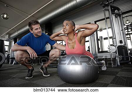 Picture - Personal trainer helping woman in health club. Fotosearch