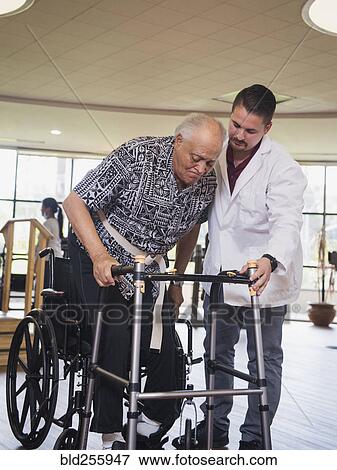 Physical therapist helping man in wheelchair use walker View Large Photo Image Stock Photo - Physical therapist helping man in wheelchair use walker. Fotosearch