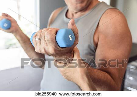 Stock Image - Physical therapist helping man lifting weights. Fotosearch