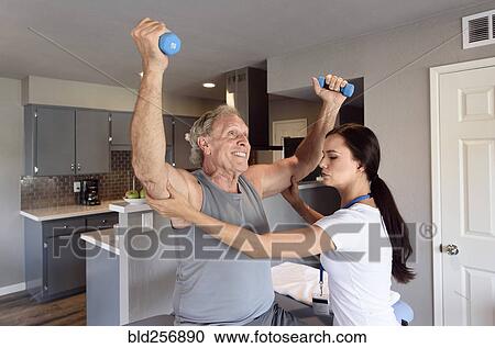 Stock Image - Physical therapist helping man lifting dumbbells. Fotosearch