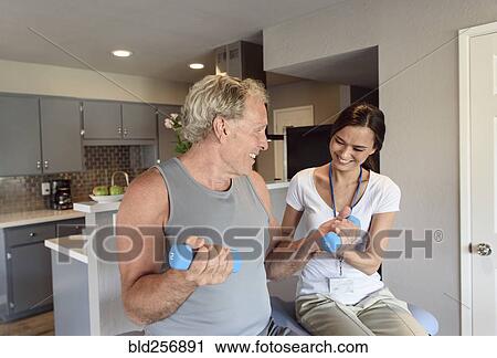 Stock Image - Physical therapist helping man lifting dumbbells. Fotosearch