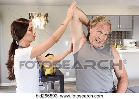 Stock Image - Physical therapist helping man stretch arm. Fotosearch