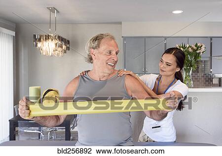 Stock Image - Physical therapist helping man using resistance band. Fotosearch
