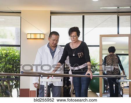 Stock Image - Physical therapist helping walking patient. Fotosearch