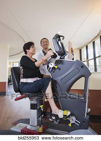 Stock Image - Physical therapist watching patient on exercise machine. Fotosearch