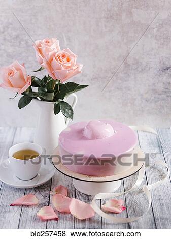Stock Photo - Pink cake with tea near vase of flowers. Fotosearch