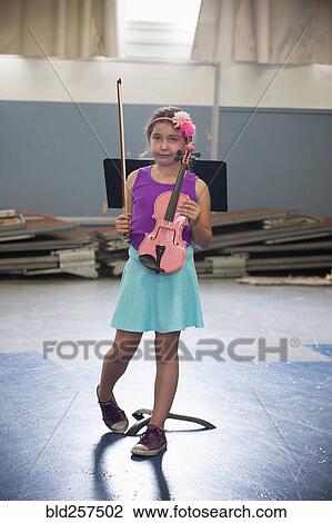 Stock Image - Portrait of awkward Hispanic girl holding pink violin. Fotosearch