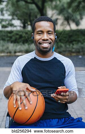 Portrait of Black man listening to earbuds and holding basketball View Large Photo Image Picture - Portrait of Black man listening to earbuds and holding basketball. Fotosearch