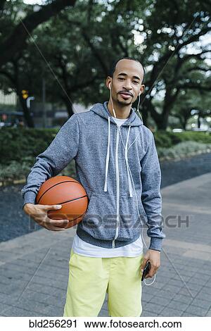 Stock Image - Portrait of Black man listening to earbuds and holding basketball. Fotosearch