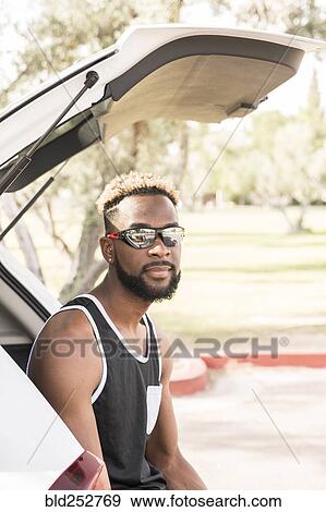 Stock Photo - Portrait of Black man wearing sunglasses in car hatchback. Fotosearch