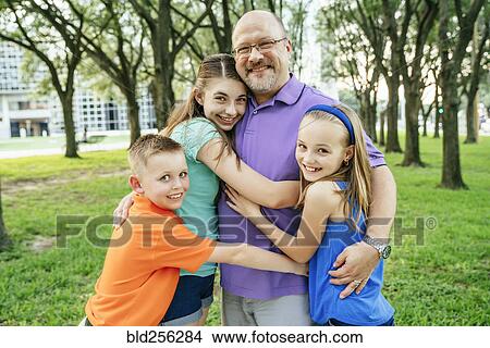 Portrait of Caucasian boy and girls hugging father in park View Large Photo Image Picture - Portrait of Caucasian boy and girls hugging father in park. Fotosearch