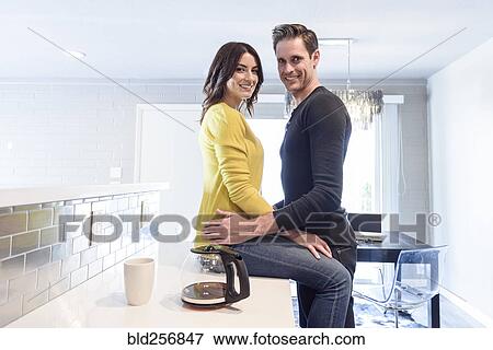 Stock Photo - Portrait of Caucasian couple embracing on kitchen counter. Fotosearch