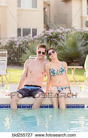 Stock Photo - Portrait of Caucasian couple sitting at edge of swimming pool. Fotosearch
