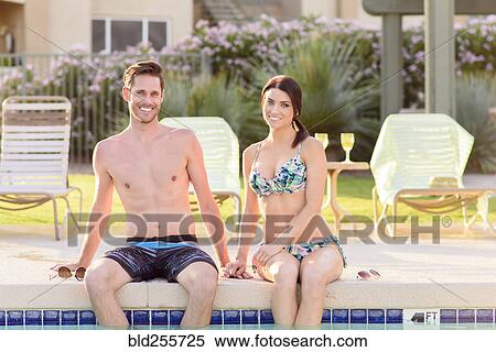 Stock Photography - Portrait of Caucasian couple sitting at edge of swimming pool. Fotosearch