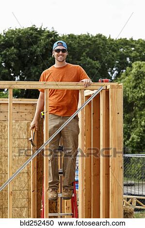Stock Image - Portrait of Caucasian man standing on ladder at construction site. Fotosearch