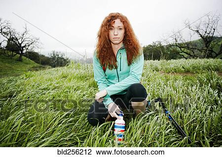 Stock Image - Portrait of crouching Caucasian woman holding bottle. Fotosearch
