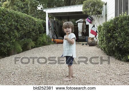 Stock Image - Portrait of curious Caucasian boy standing in driveway. Fotosearch