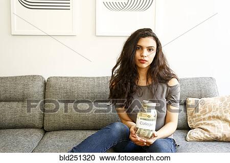 Stock Image - Portrait of mixed race woman holding jar of money for college. Fotosearch