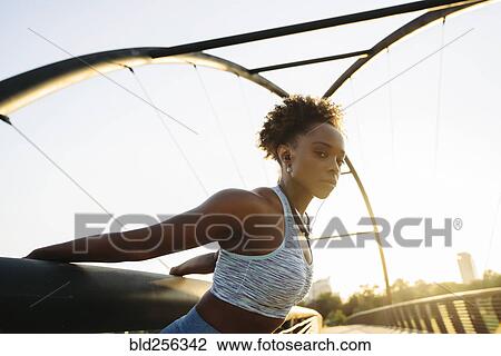 Stock Image - Portrait of mixed race woman stretching arms by pulling on railing. Fotosearch