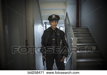 Stock Image - Portrait of older Caucasian policewoman holding gun in apartment staircase. Fotosearch